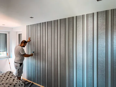 Handwerker bringt sauber eine Mustertapete an der Wand an