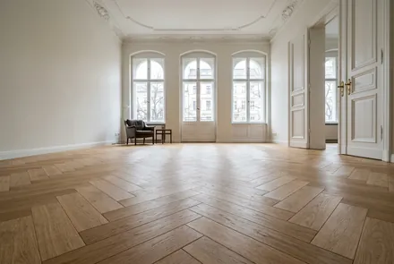 Fischgrät-Parkett in einem Altbau mit hohen Fenstern und Stuck
