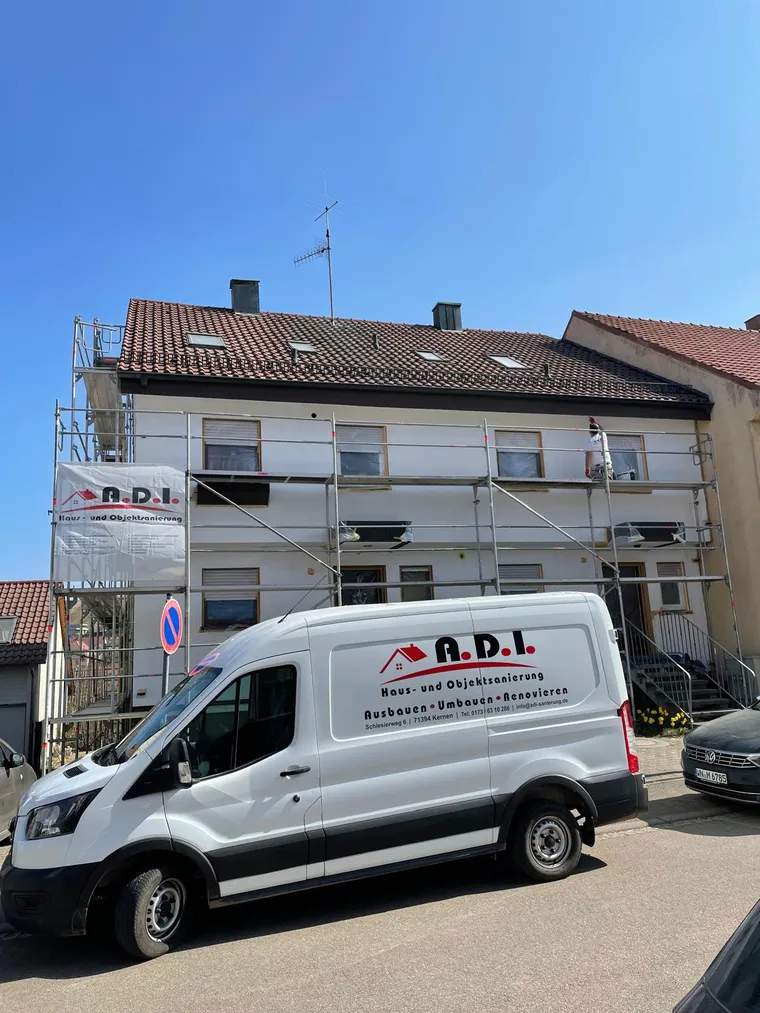 A.D.I.-Firmenwagen vor einem eingerüsteten Mehrfamilienhaus, Handwerker streicht die Fassade